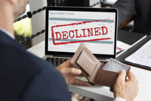 person in front of computer with declined stamp across screen and wallet open