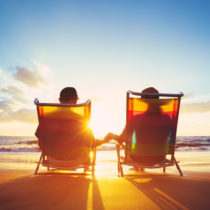 retired couple sitting on a beach during sunset